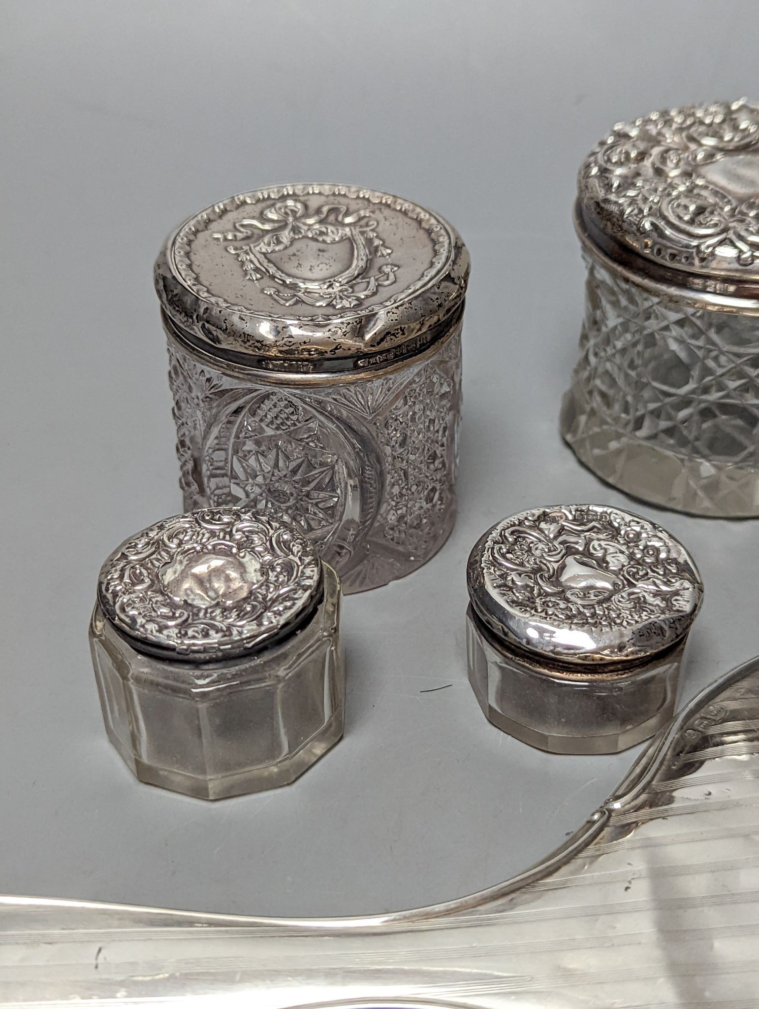 A silver mounted hand mirror, five assorted silver mounted glass toilet jars and an Indian white metal rectangular box.